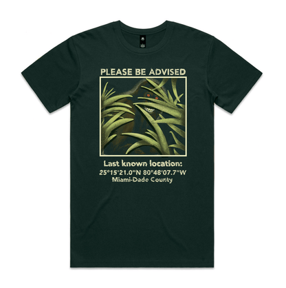 Forest green t-shirt with a picture of a skunk ape surrounded by the text 'please be advised, last known location' with coordinates in Miami-Dade County. 